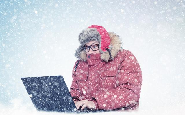 Frierender Mann sitzt im Schnee vor einem Laptop