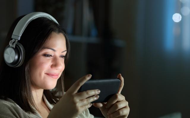 Junge Frau mit Kopfhörern streamt auf dem Handy eine Serie oder einen Film